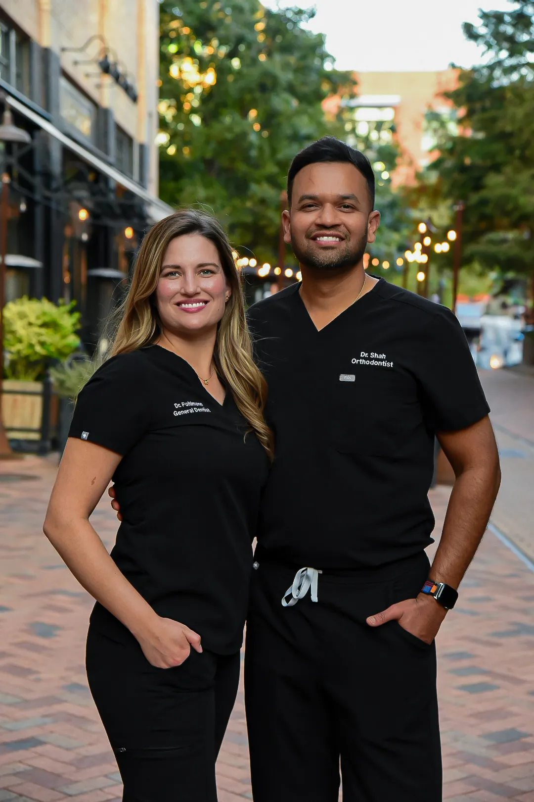 Dr. Elizabeth Pohlmann and Dr. Darshit Shah outside on a brick street, both in black scrubs