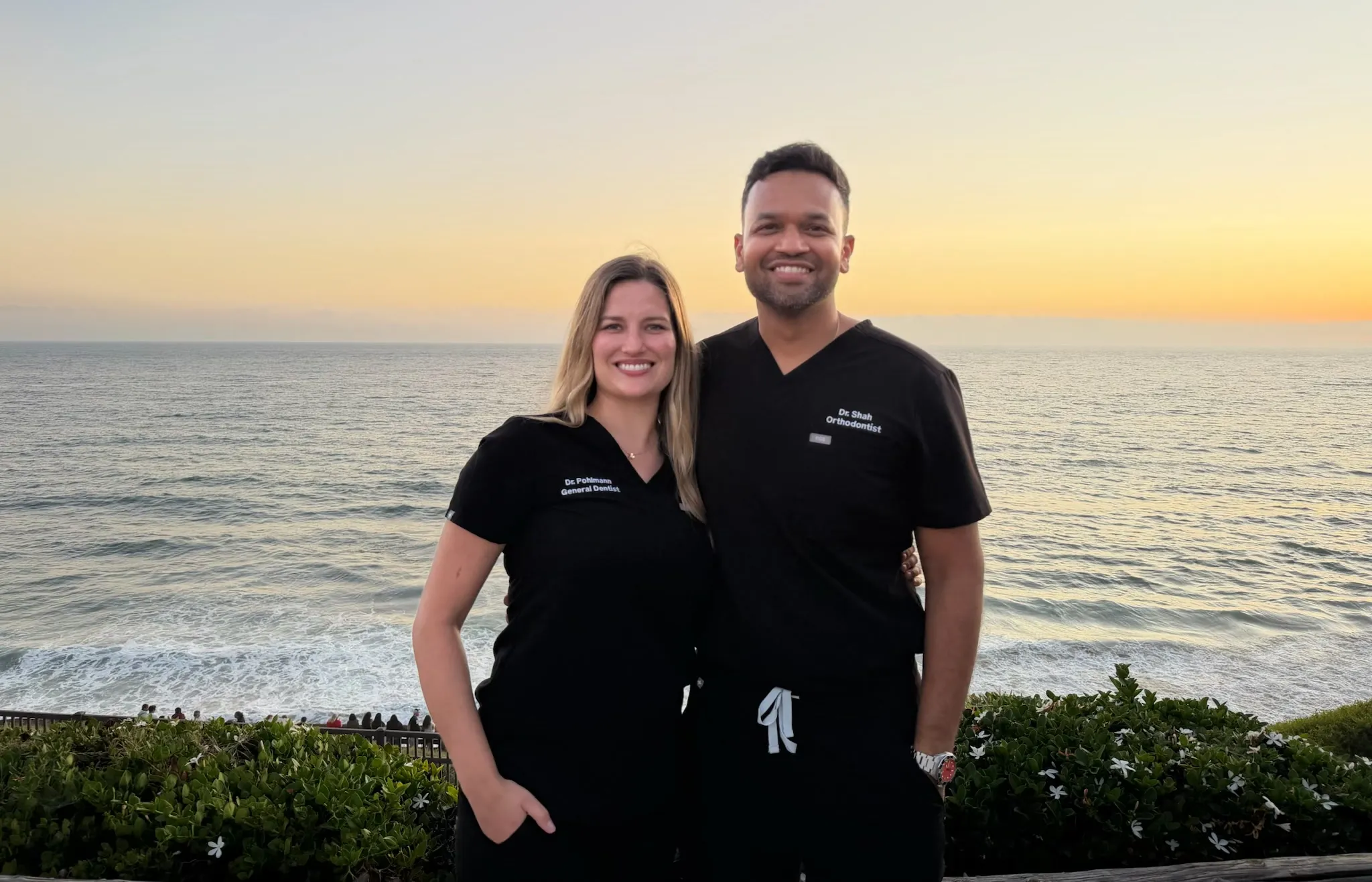 Dr. Elizabeth Pohlmann and Dr. Shah in scrubs at the shore at sunset